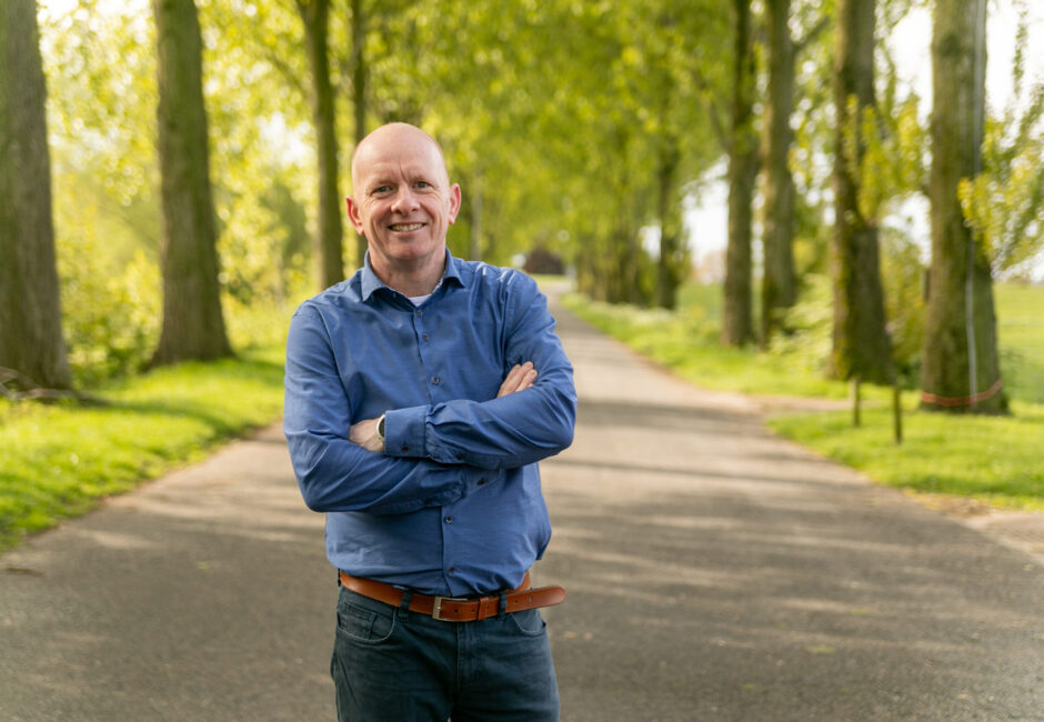 Arie lacht naar de camera terwijl hij op een weg tussen de bomen staat.