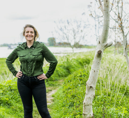 Ayla lacht naar de camera terwijl ze in het gras en tussen de bomen staat