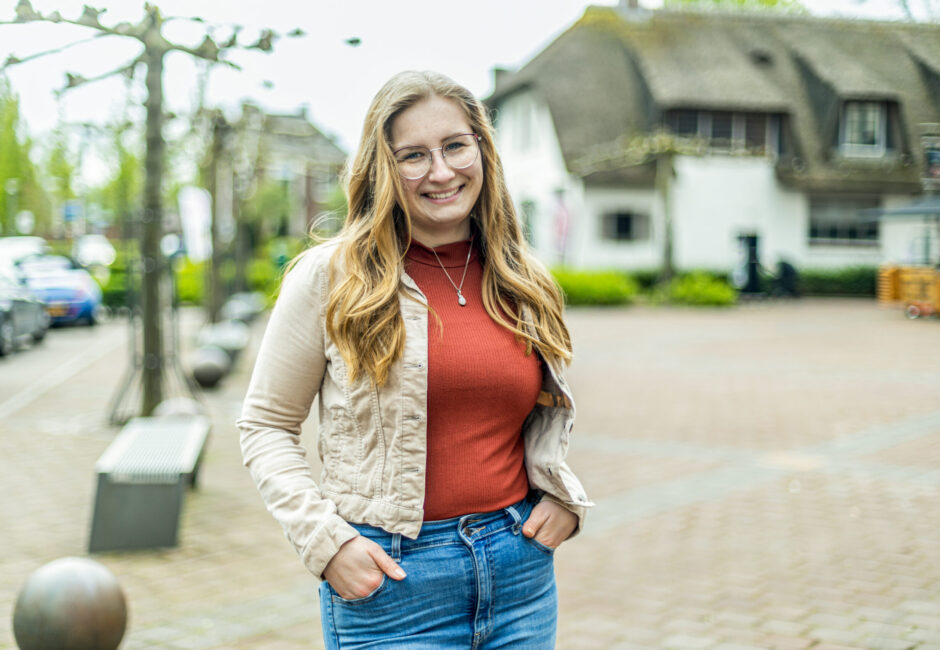 Femke kijkt lachend in de camera. Ze staat op het dorpsplein in Opheusden.