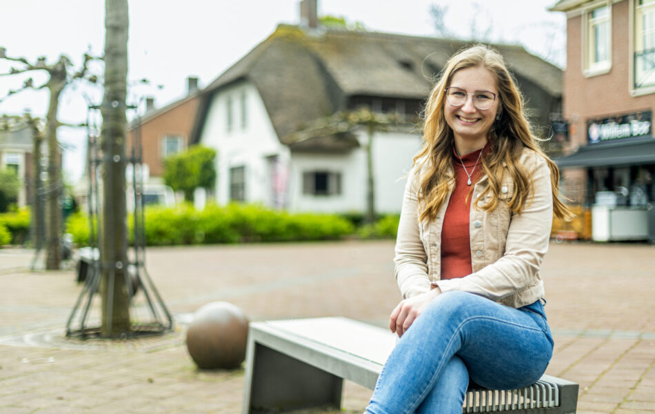 Femke zit op een bankje en lacht naar de camera.